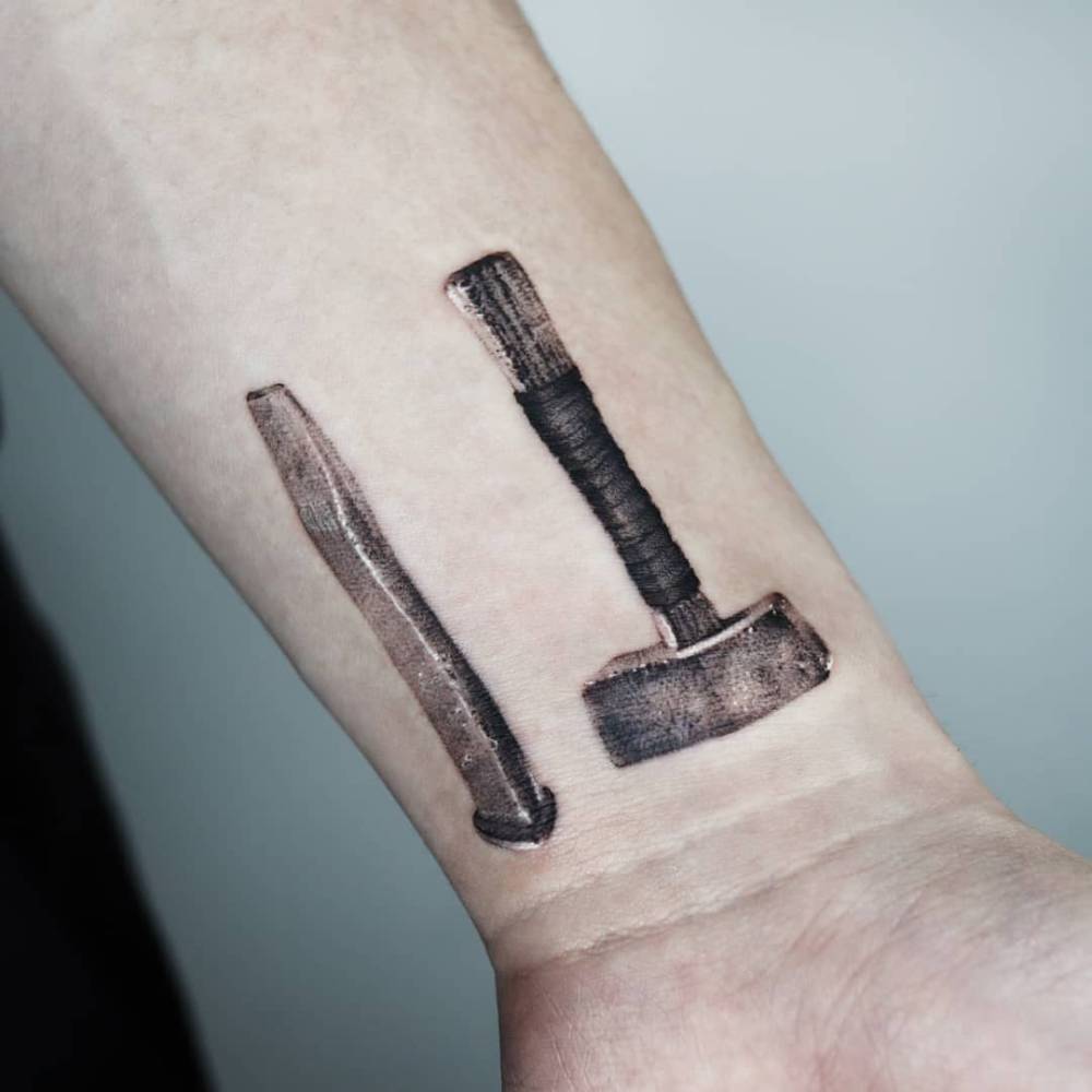 Hammer and chisel tattoo located on the wrist, micro-realistic style.