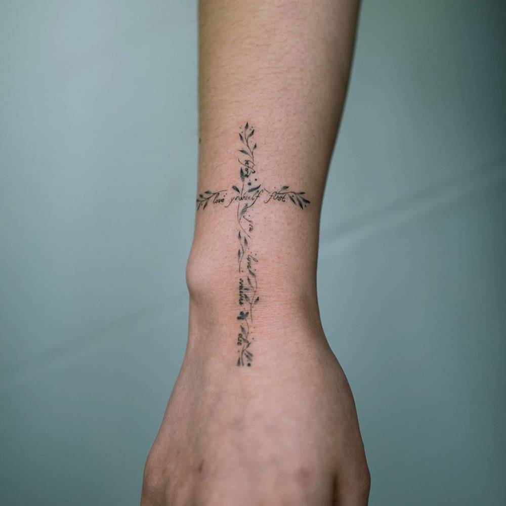 Flower cross tattoo located on the wrist, illustrative style.