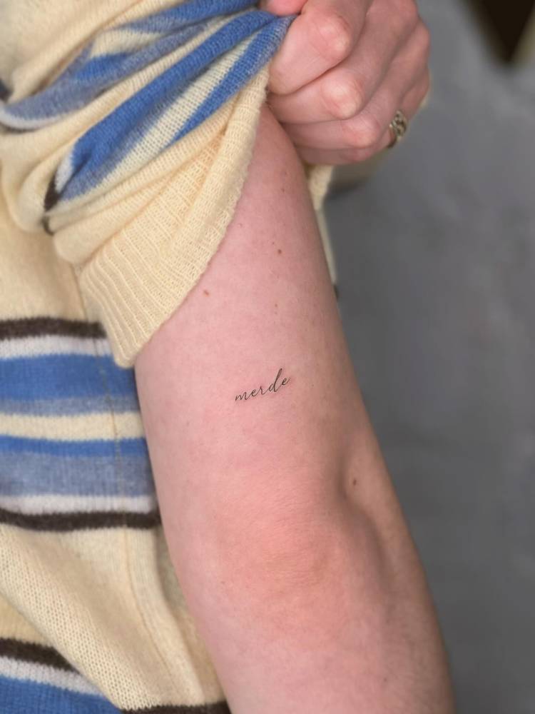 "Merde" lettering tattoo in script font done on the tricep.