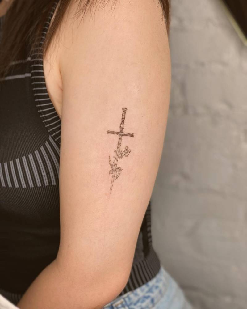 Sword and flowers tattoo in fine line style located on the upper arm.