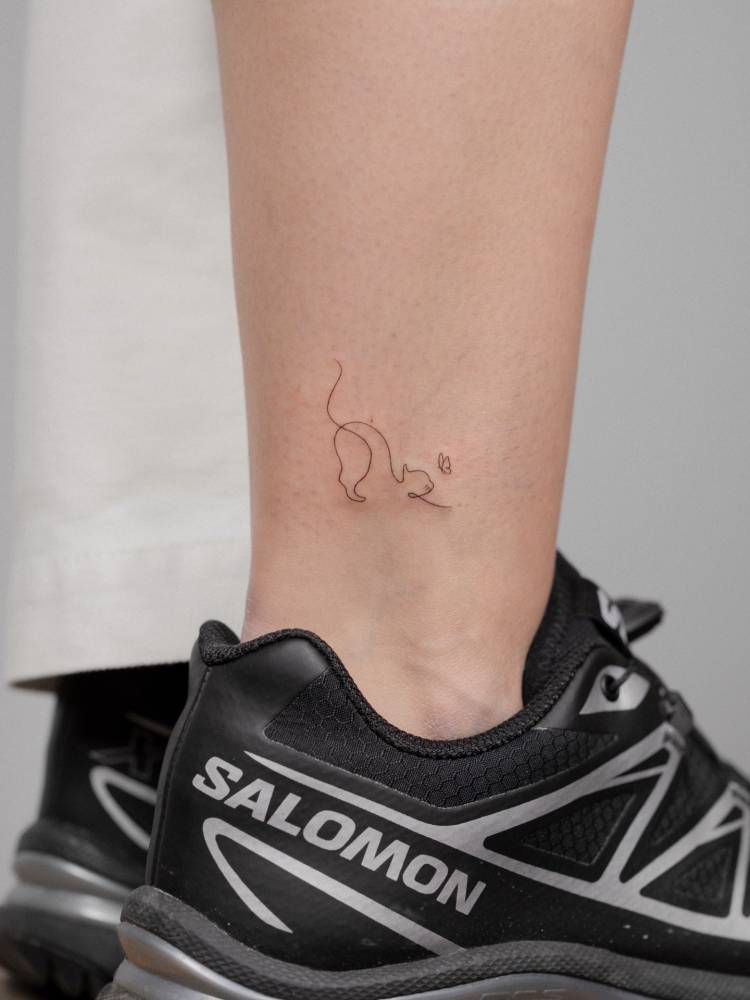 Stretching cat tattoo in fine line style located on the ankle.