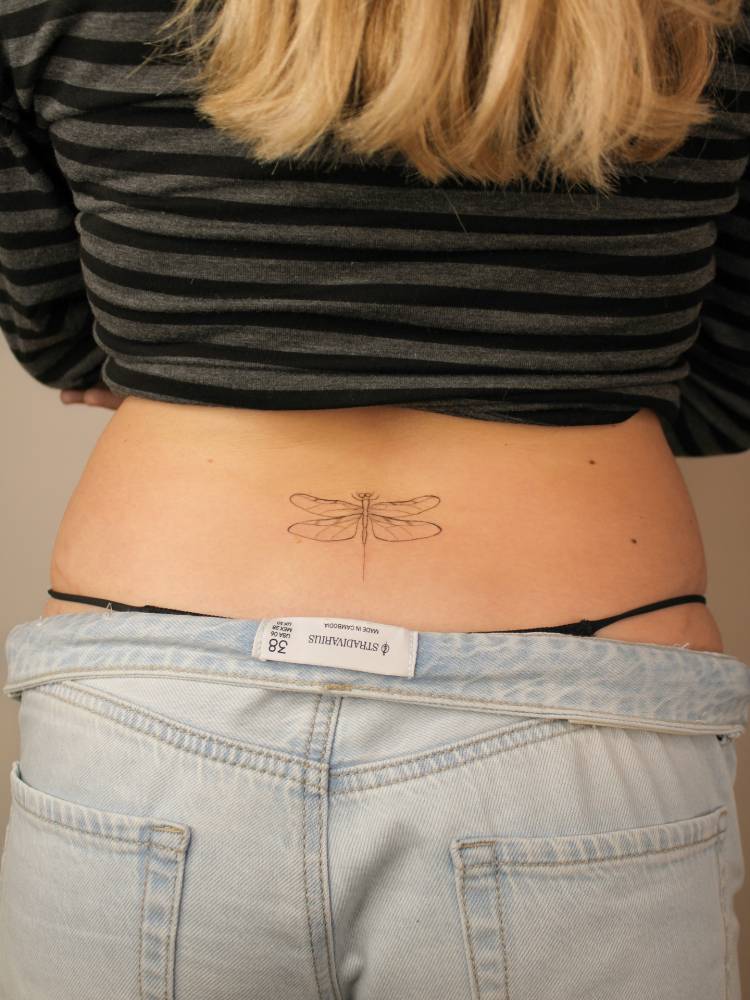 Tattoo of a dragonfly in fine line style located on the lower back.