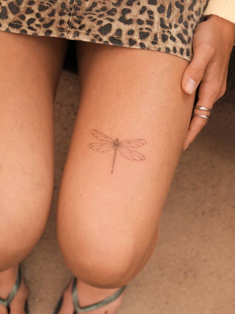 Dragonfly tattoo placed on the thigh, done in fine line style.