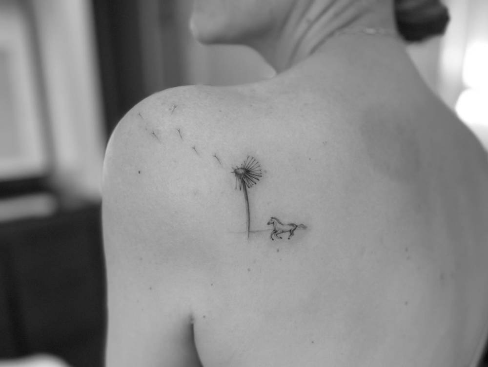 Illustrative style dandelion and horse tattoo located on the shoulder blade.
