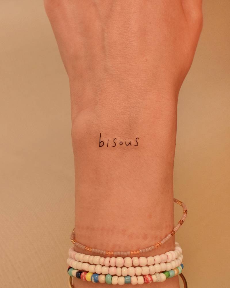 Lettering tattoo of the word "bisous" located on the wrist.