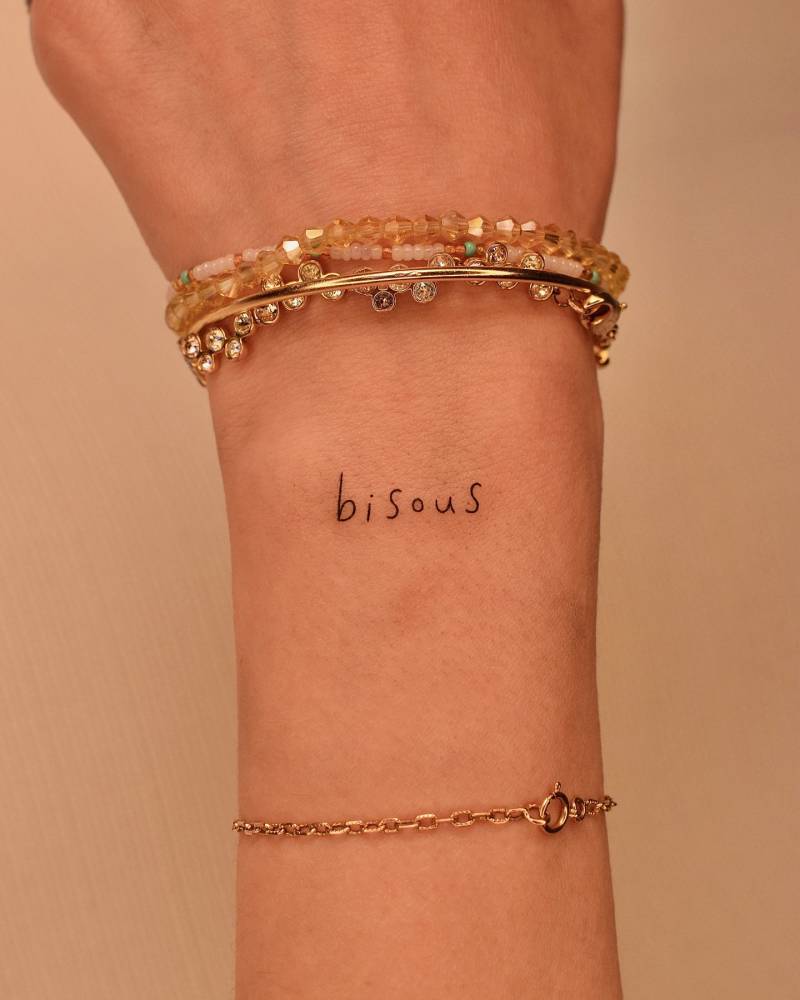 Lettering tattoo of the word "bisous" located on the wrist.