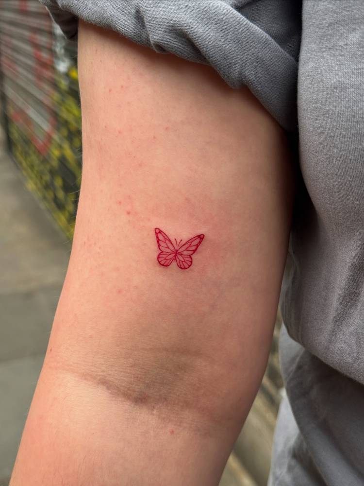 Tiny fine line red butterfly tattoo placed on the inner arm.