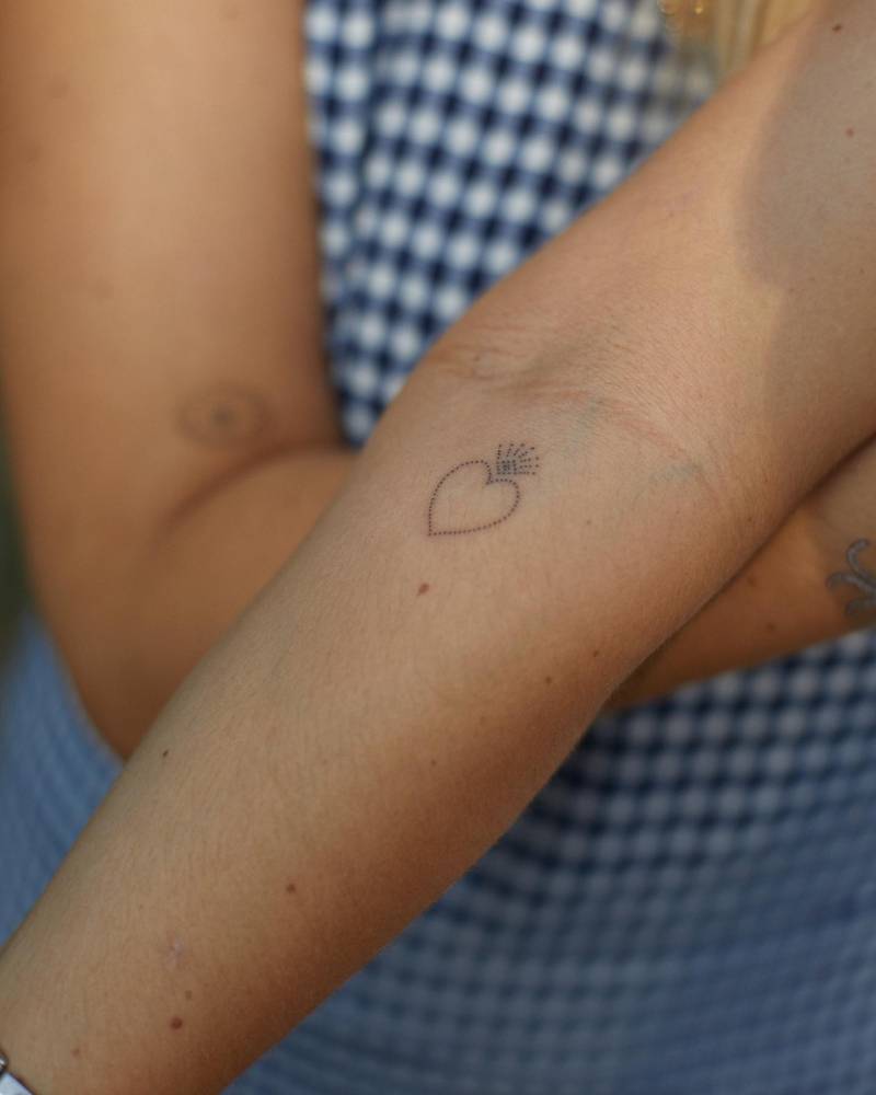 Minimalistic style flaming heart tattoo hand poked on the inner forearm.