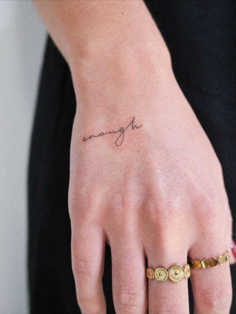Handwritten font word "enough" lettering tattoo located on the hand.