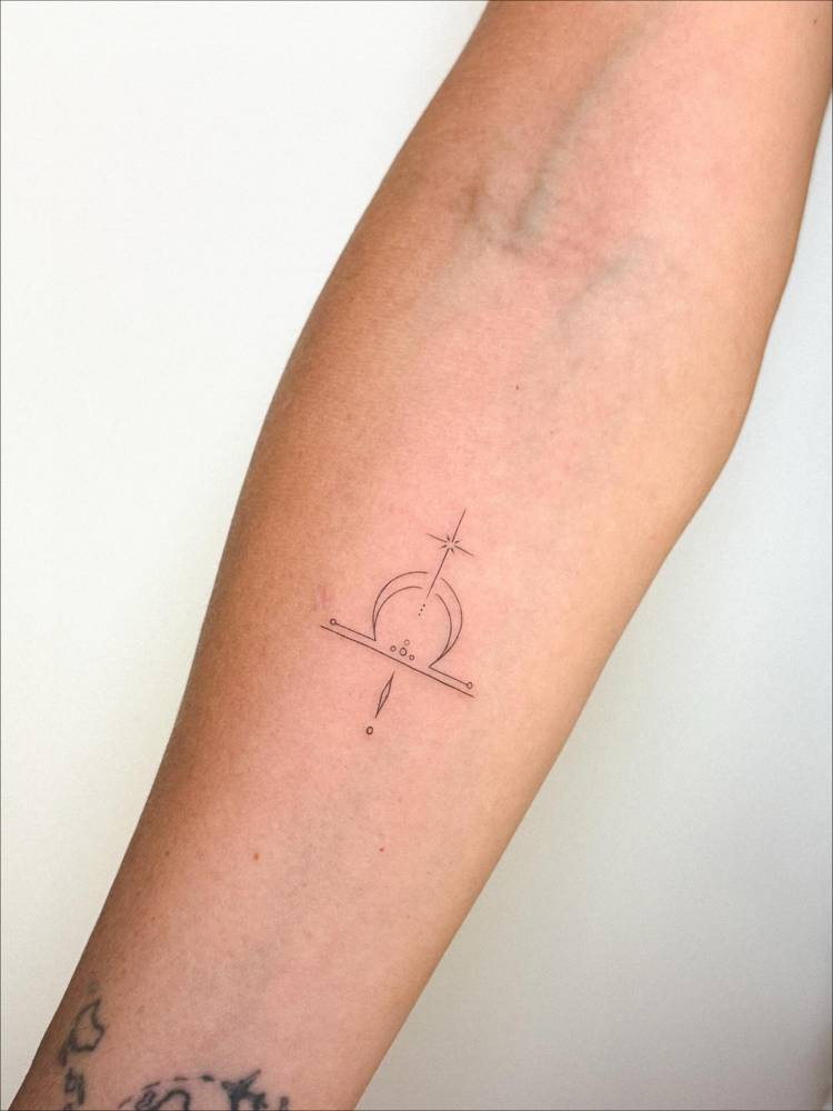 Fine line style Libra zodiac symbol tattooed on the inner forearm.