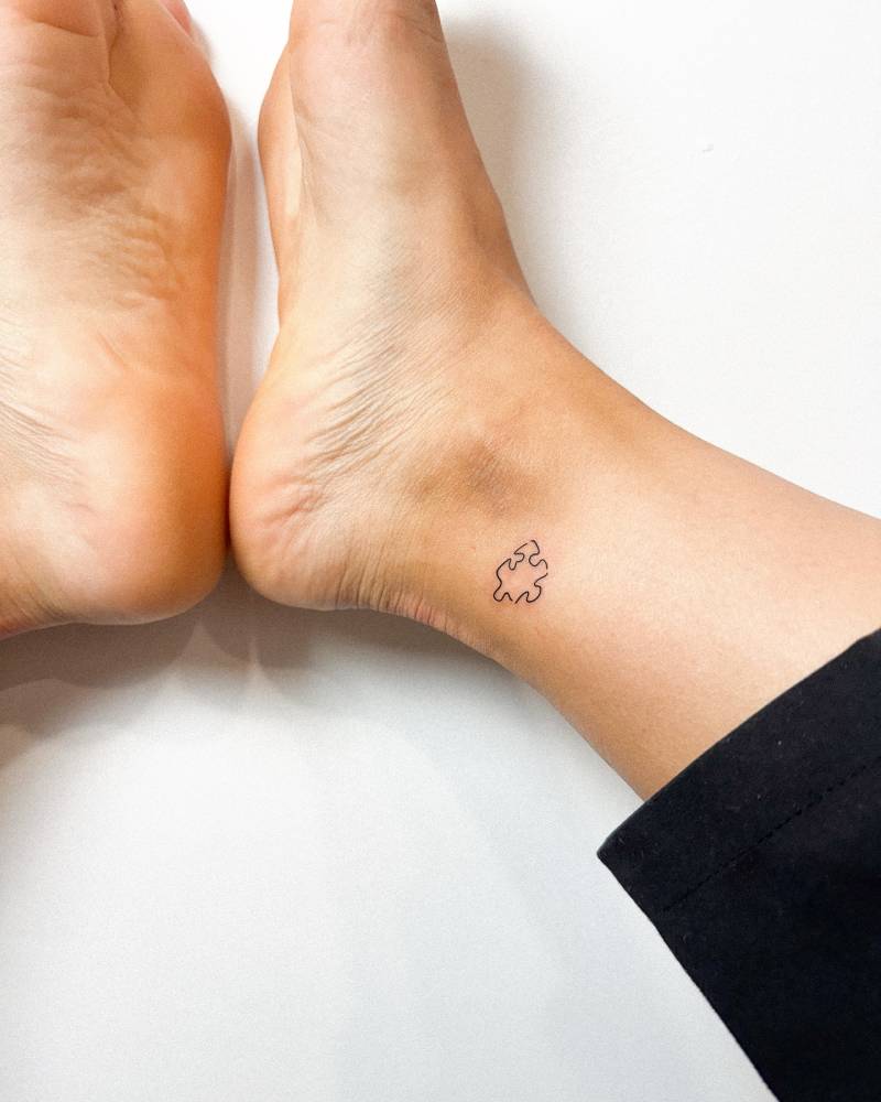 Tiny minimalistic puzzle piece tattoo located on the ankle.