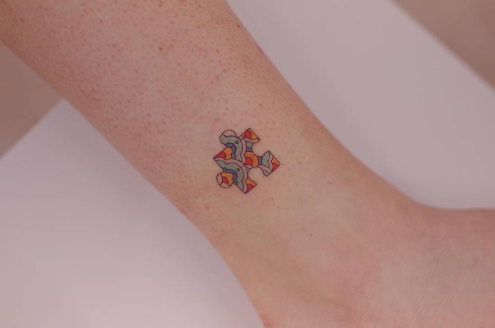 Puzzle piece tattoo in illustrative style located on the ankle.
