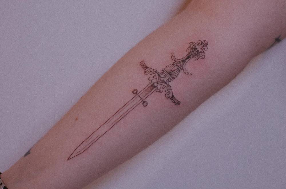 Illustrative style dagger tattoo located on the inner forearm.
