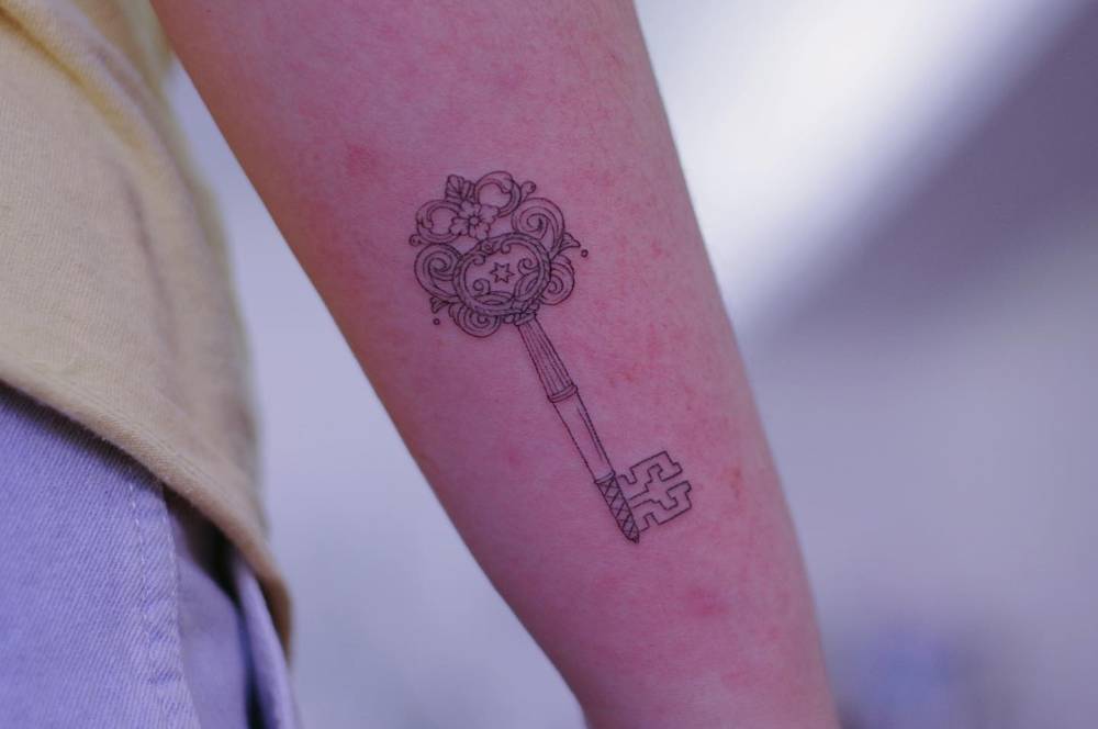 Little key tattoo located on the forearm, done in fine line style.