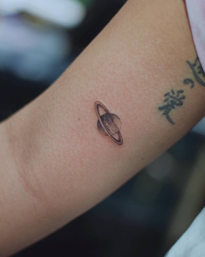 Saturn tattoo located on the inner arm, illustrative style.