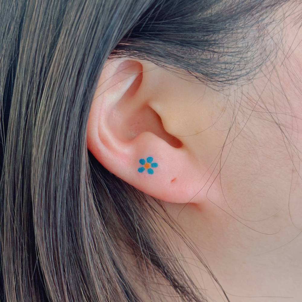 Tiny minimalistic flower tattoo located on the earlobe.