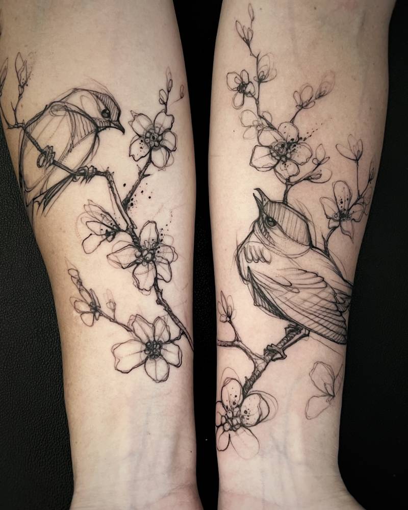 Individual matching birds on a cherry blossom branch tattoo.