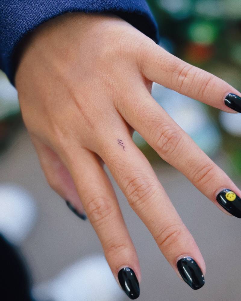 Tiny minimalistic letter "w" tattoo located on the finger.