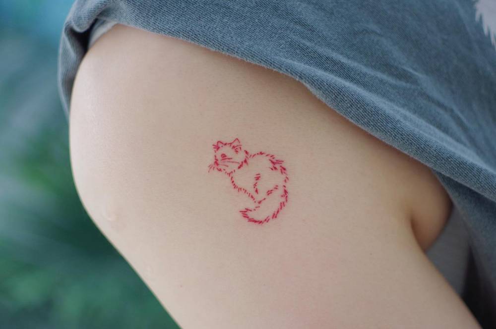 Red cat tattoo in minimalistic style located on the shoulder.