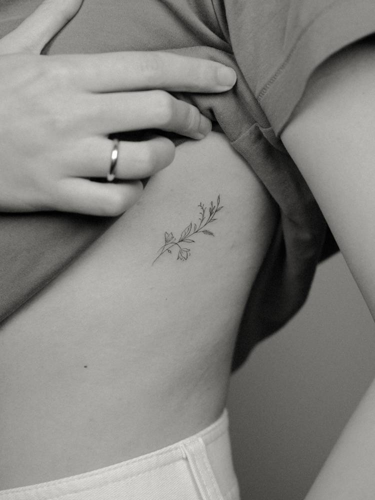 Flower branch tattoo done on the rib, fine line style.
