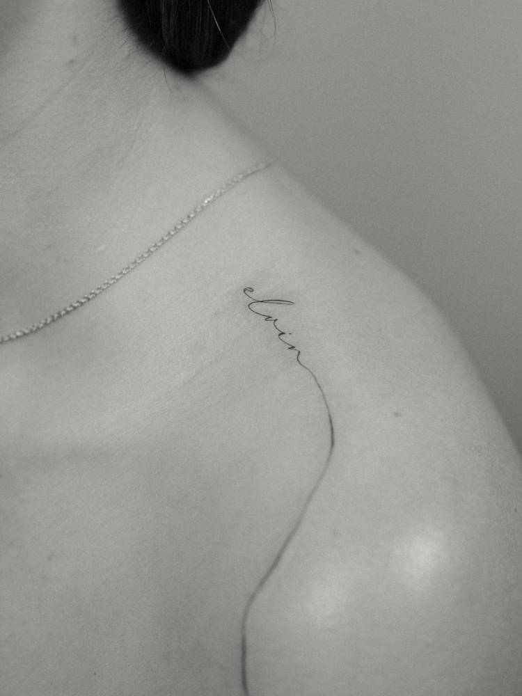 Script font name "Elvin" tattoo located on the top of shoulder.
