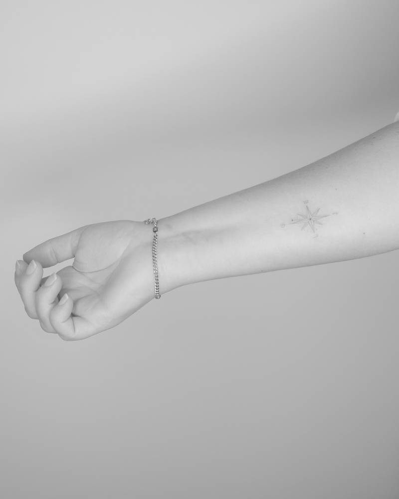 Compass rose tattoo in fine line style located on the inner forearm.