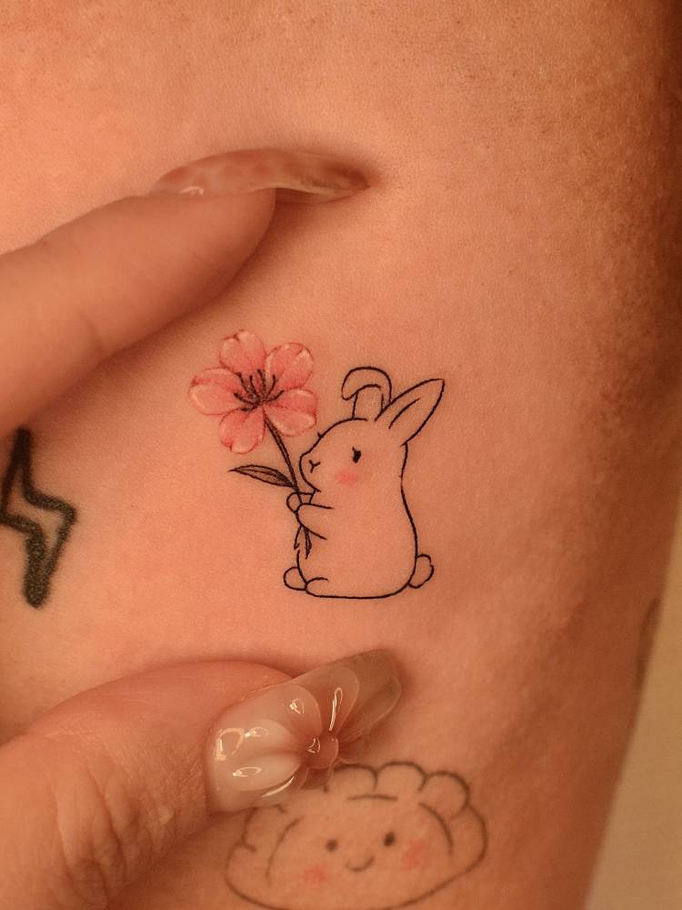 Cartoon style rabbit and cherry blossom tattoo located on the inner arm.