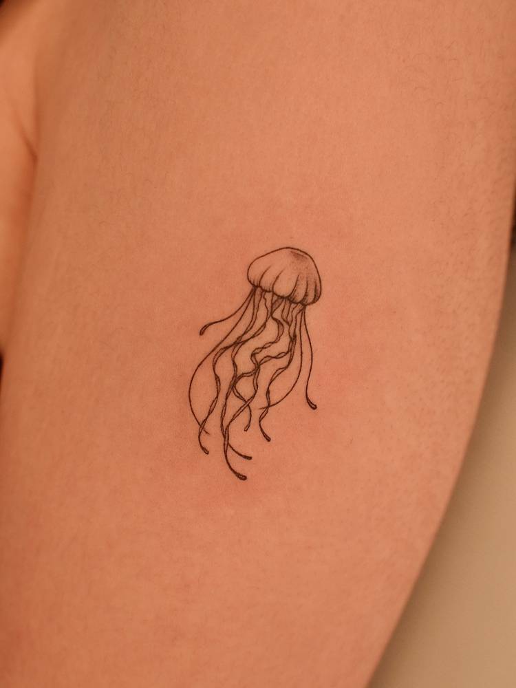 Jellyfish tattoo in fine line style placed on the upper arm.