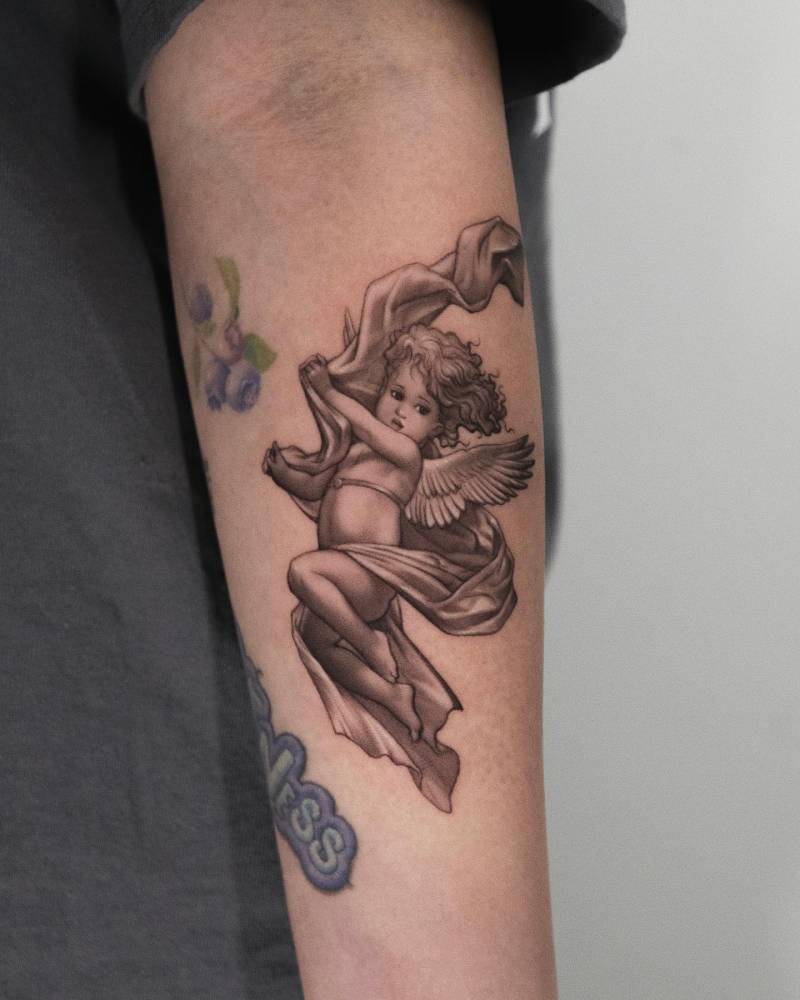 Classical style cherub tattoo located on the inner forearm.