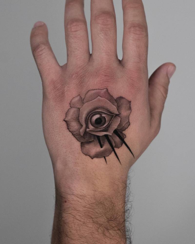 Micro-realistic style rose and eye tattoo located on the hand.