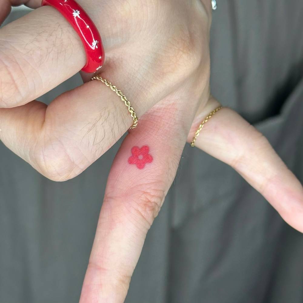 Minimalistic red flower tattoo hand poked on the finger.