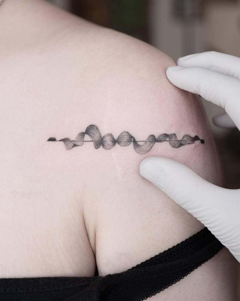 Sound wave (scar cover-up) tattoo located on the shoulder.