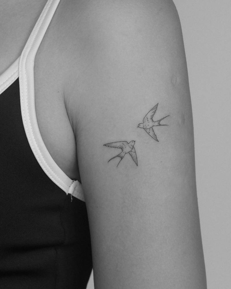 Fine line style flying swallows tattooed on the upper arm.