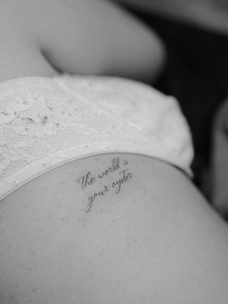 "The world is your oyster" lettering tattoo in script font located on the rib.
