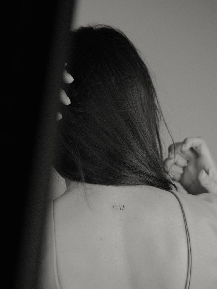 Date 12.12 in serif font tattooed on the upper back.
