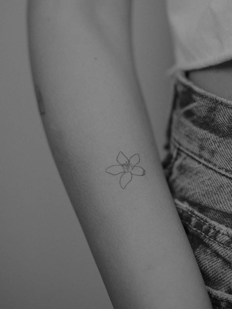 Little flower tattoo in fine line style located on the forearm.