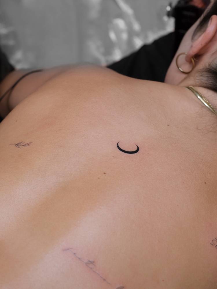 Minimalistic style crescent moon tattoo located on the upper back.