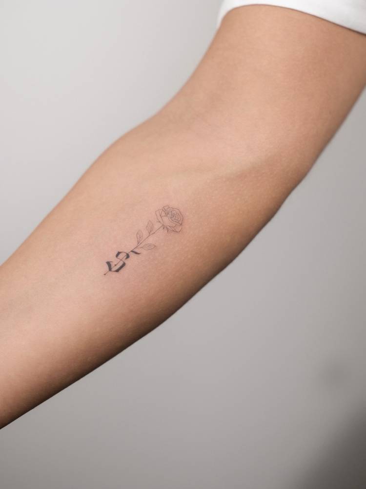 Fine line rose and gothic font letter "S" tattooed on the inner forearm.