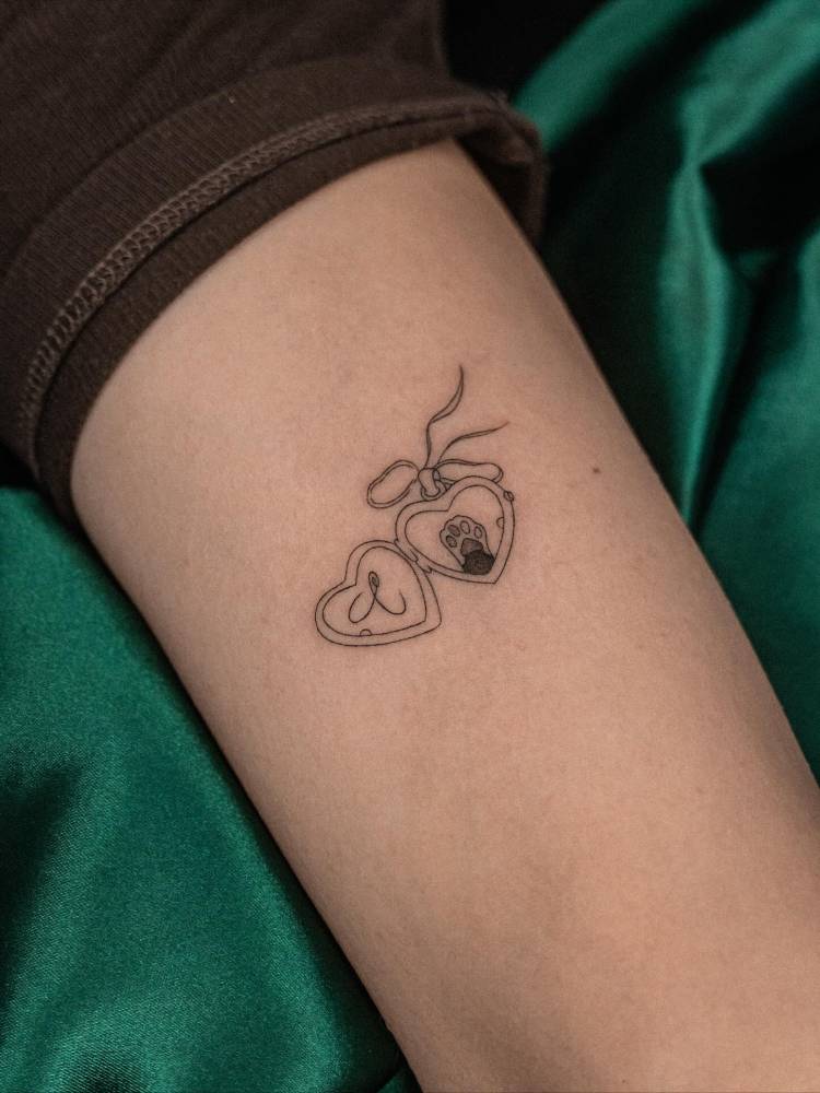 Heart pendant tattoo located on the tricep, done in illustrative style.