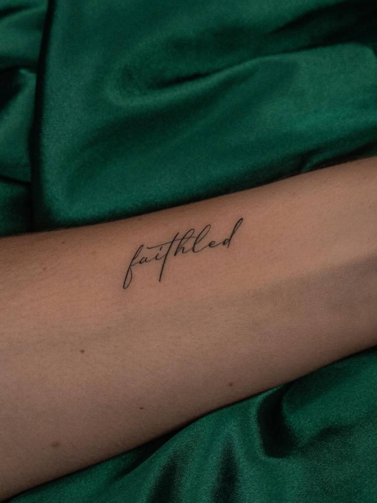 "Faithled" lettering tattoo located on the wrist.