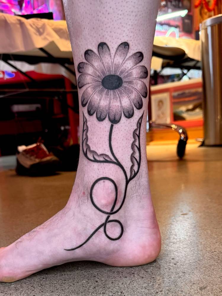 Illustrative style daisy flower tattoo located on the ankle and shin.