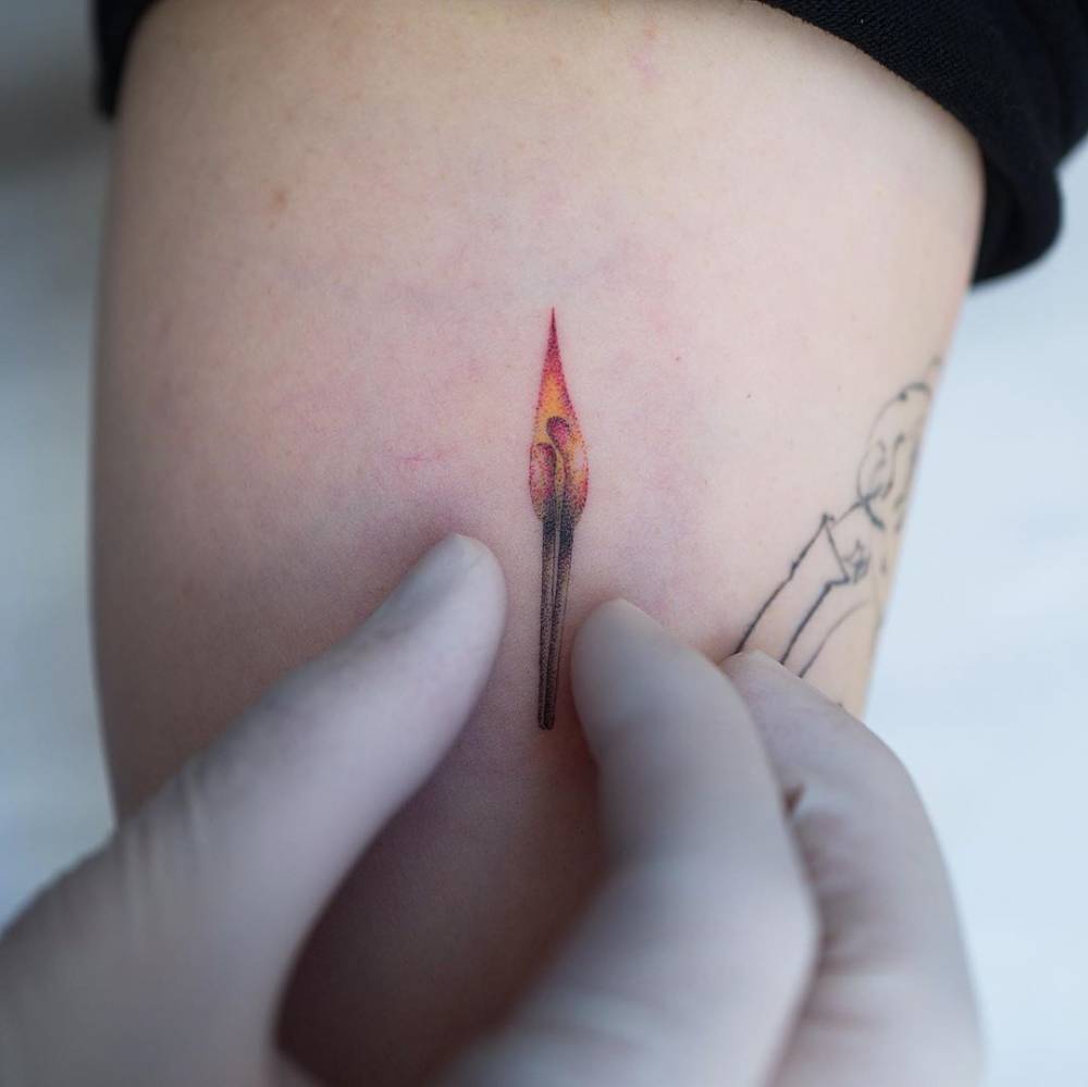 Matchstick tattoo in illustrative style located on the inner arm.
