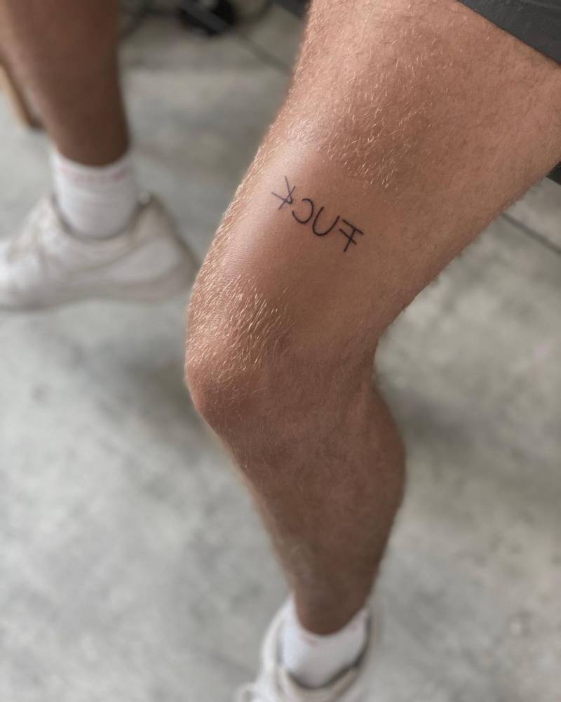 "Fuck" in mirror writing tattooed on the thigh.