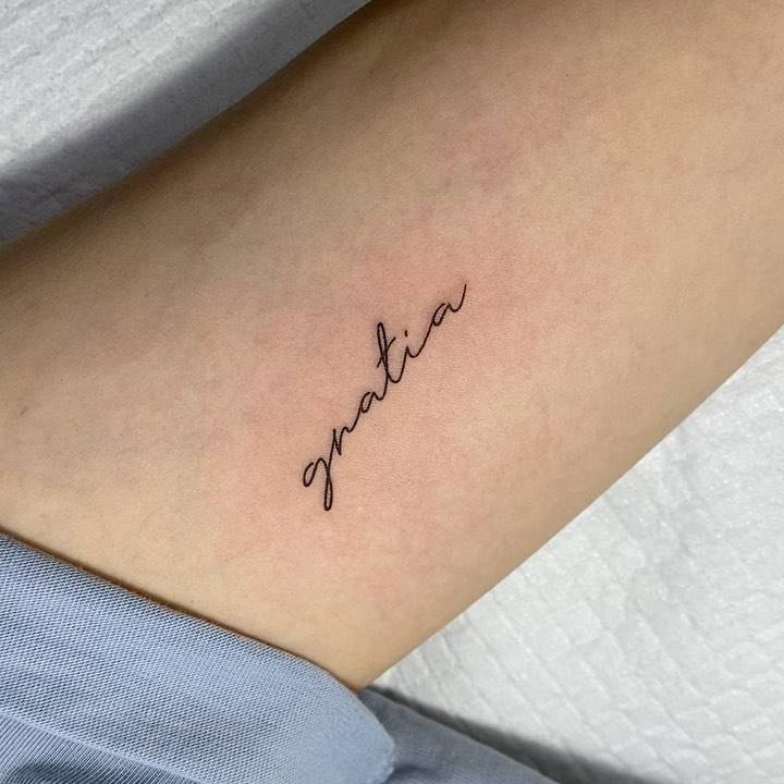 "Gratia" lettering tattoo on the inner forearm.