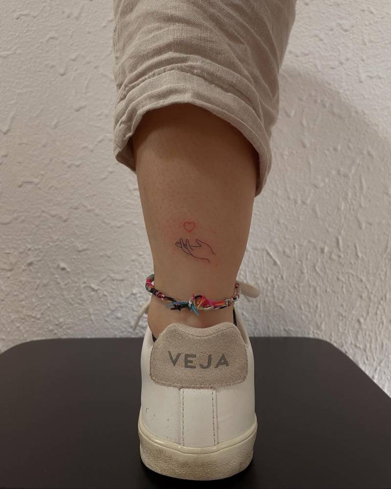 Minimalist hand and red heart tattoo on the achilles.