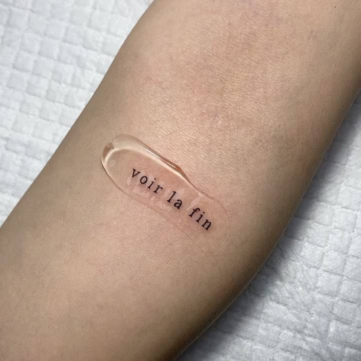 "Voir la fin" lettering tattoo on the inner forearm.