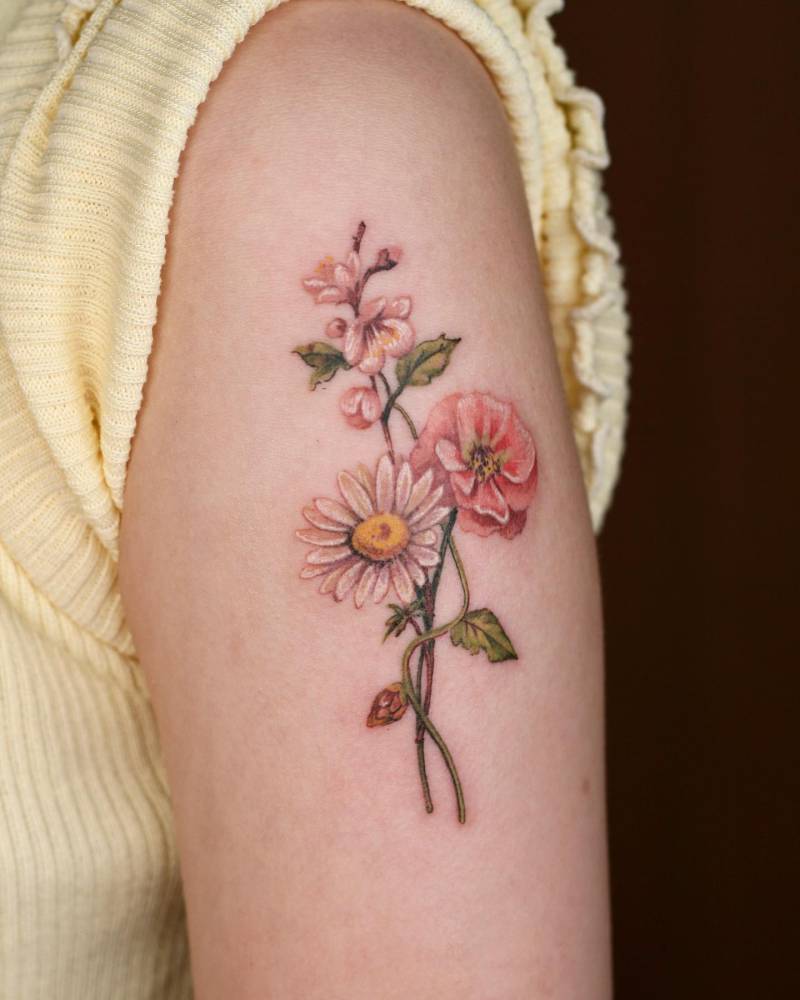 Daisy, plum blossom and moss rose tattoo located on the upper arm.