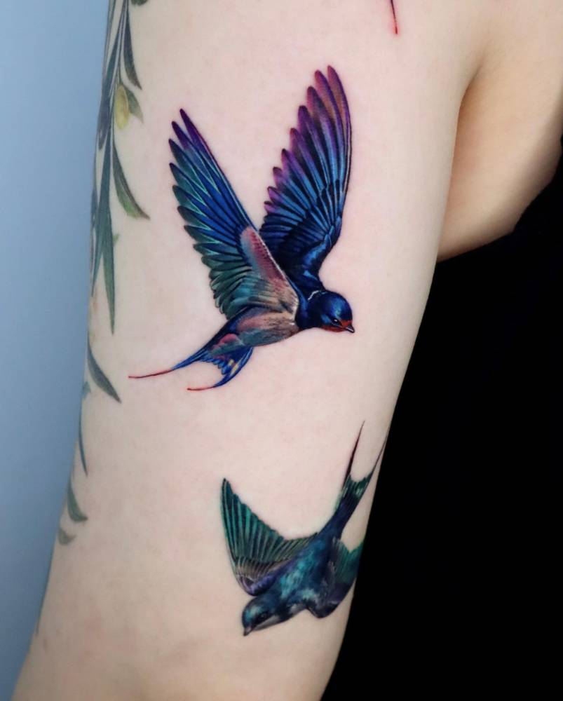 Flying swallows tattoo in realistic style located on the upper arm.
