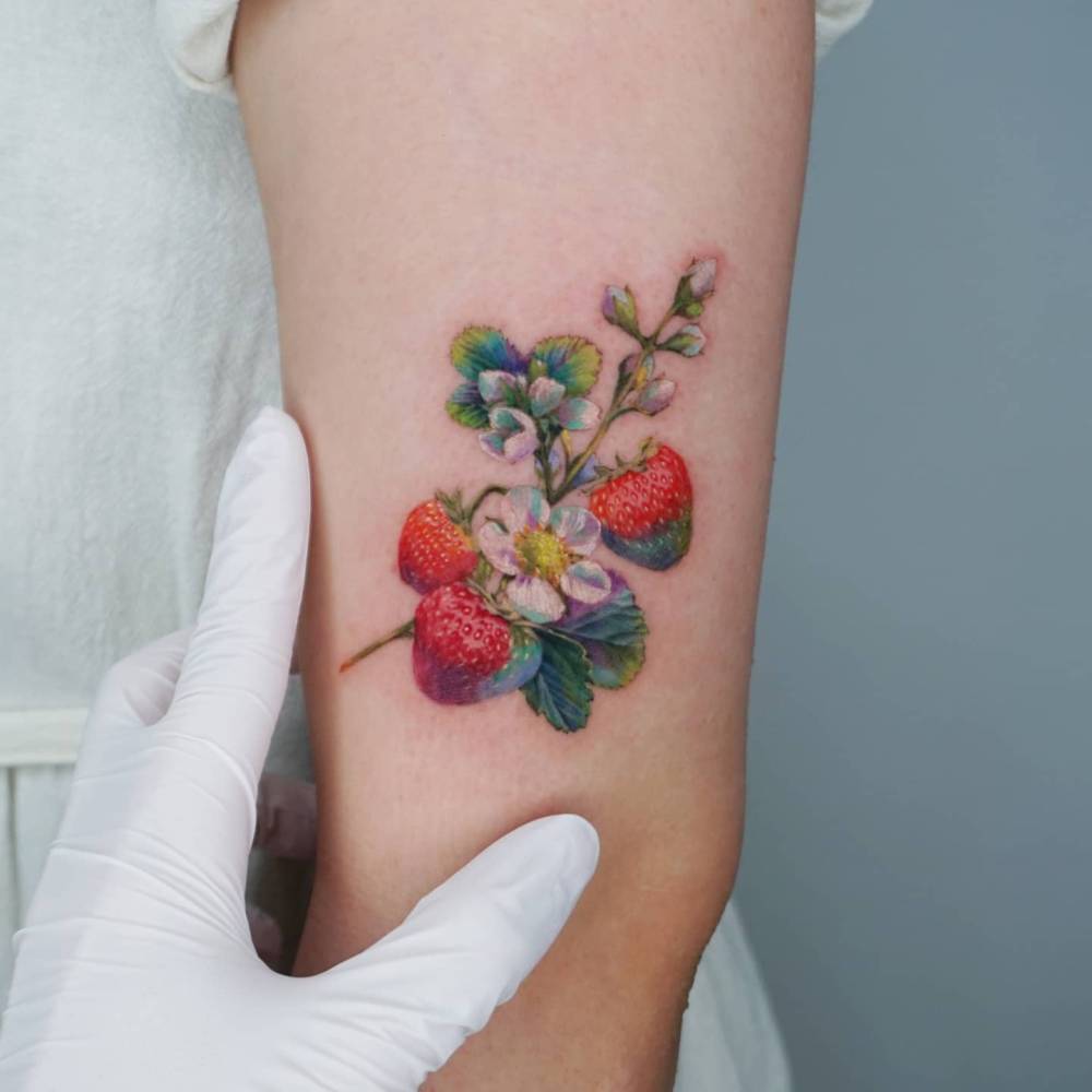 Realistic style strawberry and blossom tattoo located on the upper arm.