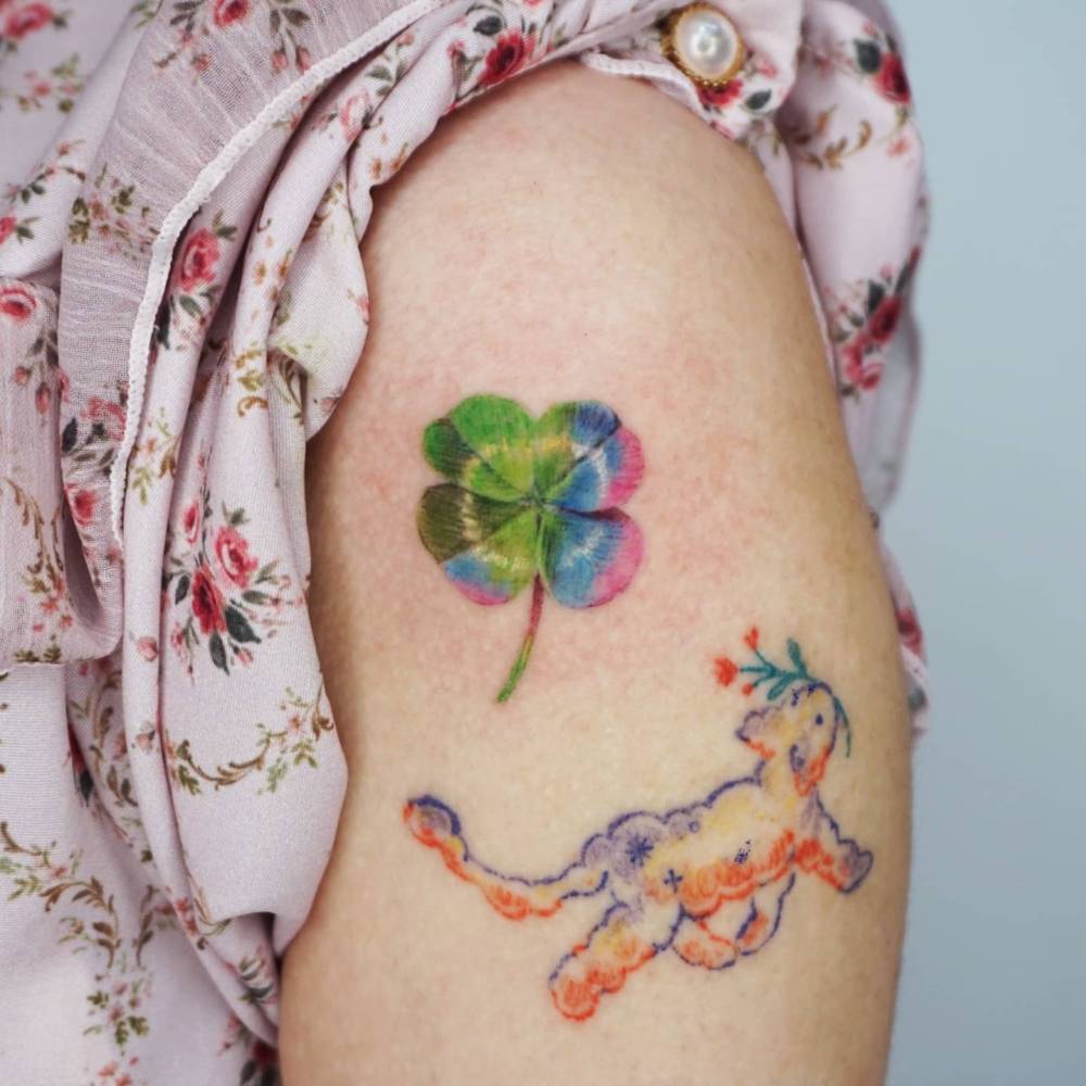 Four leaf clover tattoo in realistic style located on the upper arm.